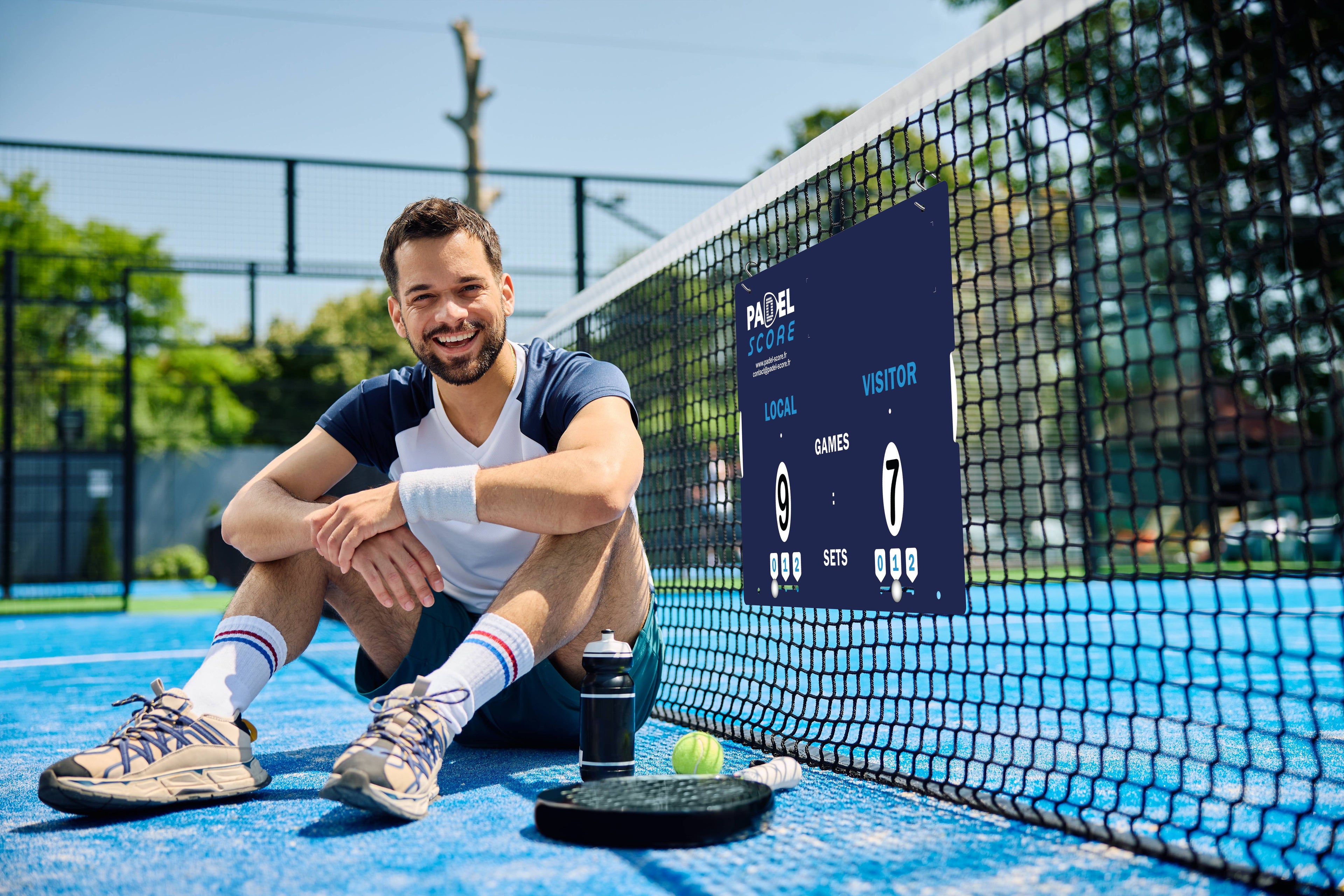 Un panneau de score accroché sur le filet d'un terrain de padel avec un joueur assis à terre